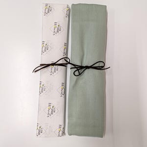 May include: A rectangular sage green fabric item folded and tied with a dark brown cord next to a white paper wrapper featuring the repeating black text A FEW SPARE MOMENTS inside diamond outlines and small yellow floral accents.