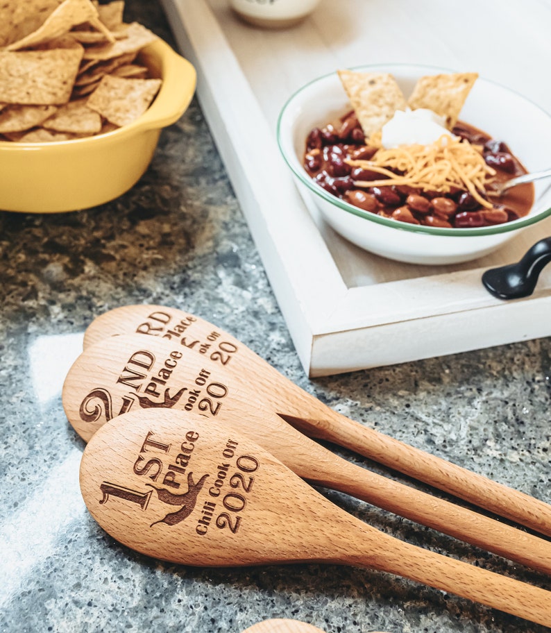 Peut inclure: Trois cuill&egrave;res en bois avec du texte grav&eacute;, indiquant "1st Place Chili Cook Off 2020", "2nd Place Cook Off 2020" et "3rd Place Cook Off 2020".