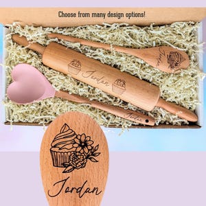 May include: A kitchen utensil set in a box with shredded paper, including a wooden rolling pin, a wooden spoon, and a pink silicone heart-shaped spatula. Each wooden item is engraved with the name Jordan and a cupcake graphic. Text reads: Choose from many design options!