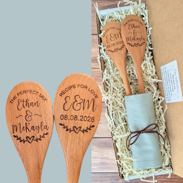 May include: Two light brown wooden spoons with laser-engraved text and heart designs. One spoon reads THE PERFECT MIX Ethan & McKayla, the other RECIPE FOR LOVE E&M 08.08.2026. The spoons are nestled in a cardboard box with shredded paper filler.
