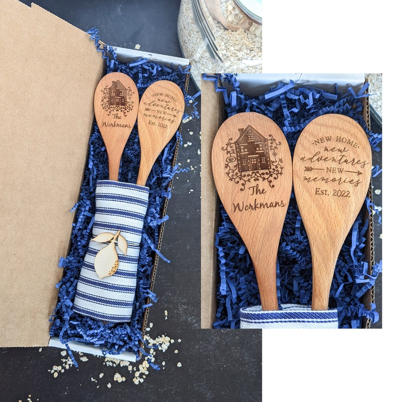 May include: Two wooden spoons with a house design and the text "The Workmans" and "New Home, New Adventures, New Memories Est. 2022" are displayed in a blue and white gift box with blue tissue paper.