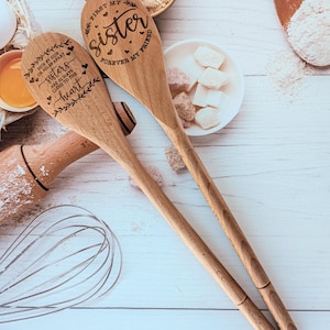 May include: Two light brown wooden spoons with laser-engraved text and decorative leaf and heart motifs. One spoon reads "First my sister, forever my friend," and the other reads "Side by side or miles apart, sisters are always close to the heart."