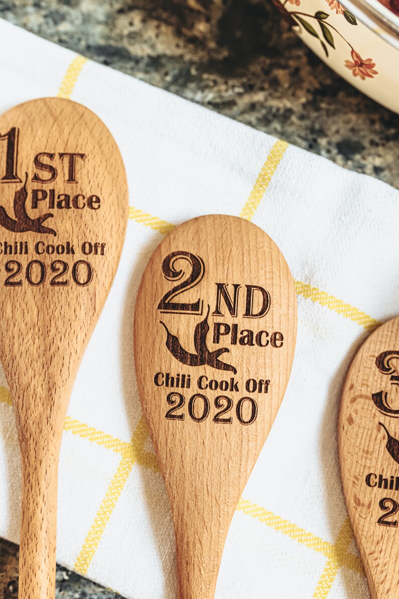 Peut inclure: Trois cuill&egrave;res en bois avec du texte grav&eacute;. Les cuill&egrave;res sont &eacute;tiquet&eacute;es "1&egrave;re place", "2&egrave;me place" et "3&egrave;me place" avec le texte "Chili Cook Off 2020" en dessous de chacune.