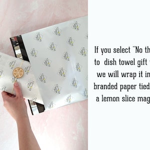 Puede incluir: Papel de regalo blanco estampado con un correo negro y plateado. Un im&aacute;n de rodaja de lim&oacute;n est&aacute; atado al papel. El texto dice: "Si selecciona 'No gracias al envoltorio de regalo de pa&ntilde;o de cocina, lo envolveremos en nuestro papel de marca atado con un im&aacute;n de rodaja de lim&oacute;n.'"