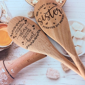 May include: Two light brown wooden spoons with laser-engraved text and heart designs. One spoon reads, "First my sister, forever my friend." The other spoon reads, "Side by side or miles apart, sisters are always close to the heart."