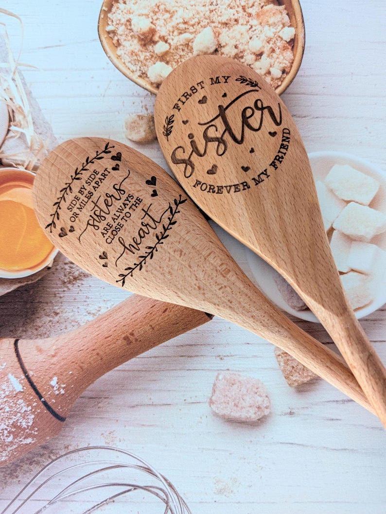 May include: Two light brown wooden spoons with laser-engraved text and heart designs. One spoon reads, "First my sister, forever my friend." The other spoon reads, "Side by side or miles apart, sisters are always close to the heart."