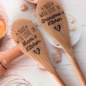 May include: Two light brown wooden spoons with laser-engraved text and heart graphics. One spoon reads "MADE WITH LOVE IN Mom's Kitchen" and the other reads "MADE WITH LOVE IN Grandma's Kitchen" with decorative flourishes.