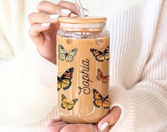 May include: A clear glass tumbler with a bamboo lid and a straw. The tumbler is filled with iced coffee and has a design of butterflies and the name "Sophia" on the side.