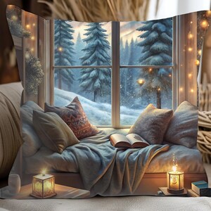 May include: A decorative pillow featuring a cozy winter scene. The image shows a window overlooking a snowy forest, with pillows, a blanket, and an open book. Lit candles and fairy lights add warmth to the scene.