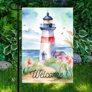 May include: A watercolor garden flag featuring a lighthouse with red and white stripes, a blue roof, and the word "Welcome" in script. The flag depicts a coastal scene with flowers, grass, and a blue sky.