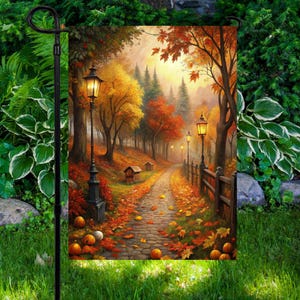 May include: A garden flag with an autumnal landscape. The image shows a path through a forest with trees in shades of orange, yellow, and red. The path is lined with lampposts and pumpkins. The scene evokes a sense of warmth and tranquility.