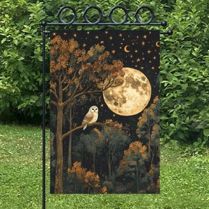 Puede incluir: Una bandera de jardín con una escena de bosque nocturno con una gran luna llena, estrellas y un búho posado en la rama de un árbol. La bandera tiene un fondo negro con detalles dorados y marrones, creando un diseño caprichoso y encantador.