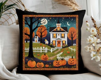Puede incluir: Cojín decorativo negro con una escena de Halloween. El diseño incluye una casa blanca con detalles en naranja, calabazas, árboles y una luna llena. El cojín tiene un borde naranja y negro.