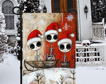 Puede incluir: Una bandera de jardín decorativa con tres esqueletos de dibujos animados con gorros de Papá Noel, en un trineo. El fondo es una mezcla de rojo y beige con acentos de copos de nieve, creando una escena festiva navideña.