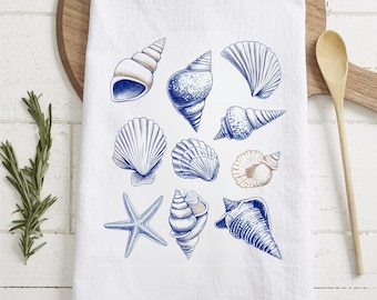 Puede incluir: Una toalla de cocina blanca con un diseño de conchas marinas azul y blanco. La toalla presenta una variedad de conchas marinas, incluyendo vieiras, caracoles y estrellas de mar.