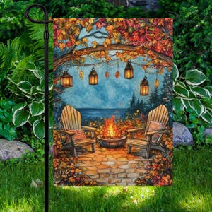 May include: A garden flag featuring a cozy autumn scene. Two wooden Adirondack chairs face a fire pit, with a backdrop of a lake and trees. Overhead, a wooden arch is adorned with lanterns and fall foliage. The flag is set in a lush green garden.