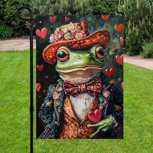 Puede incluir: Una bandera de jardín con una rana elegante con un sombrero adornado con flores, una pajarita y un traje, sosteniendo un corazón. El fondo oscuro presenta corazones rojos flotantes, creando una escena caprichosa y romántica.