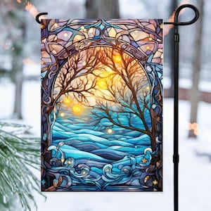 May include: A garden flag featuring a stained-glass design of a winter scene. The artwork depicts bare trees, a blue river, and a warm, glowing sun. The flag is rectangular and hangs from a black metal pole, with a snowy background.