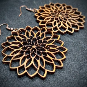 May include: A pair of wooden earrings with a mandala design. The earrings are brown and have a intricate pattern.