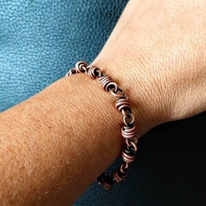 May include: A copper wire bracelet with a twisted design. The bracelet is made of two different shades of copper, one darker and one lighter.