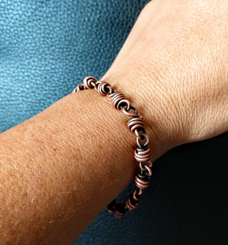 May include: A copper wire bracelet with a twisted design. The bracelet is made of two different shades of copper, one darker and one lighter.
