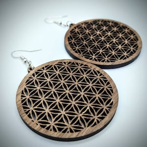 May include: A pair of wooden earrings with a circular design featuring a geometric pattern. The earrings are made of dark wood and have silver hooks.