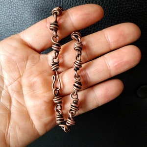 May include: A copper wire bracelet with a clasp closure. The bracelet is made of multiple small coils of wire.