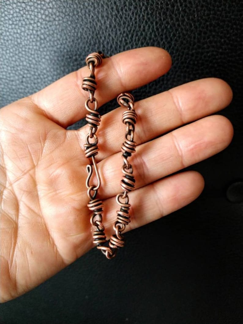 May include: A copper wire bracelet with a clasp closure. The bracelet is made of multiple small coils of wire.