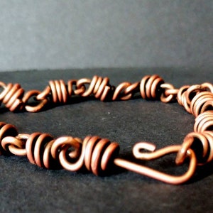 May include: A copper wire bracelet with a coiled design. The bracelet has a hook clasp.