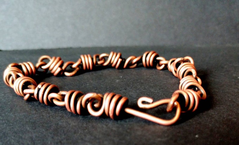 May include: A copper wire bracelet with a coiled design. The bracelet has a hook clasp.