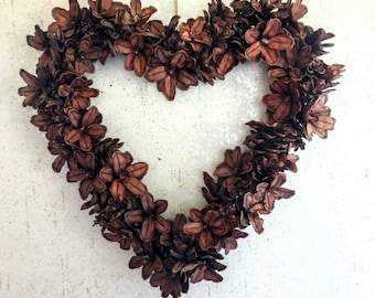 May include: A brown heart-shaped wreath made of dried flowers. The wreath is hanging on a white wall.