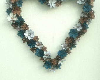 May include: A heart-shaped wreath made of pine cones painted in shades of blue, brown, and white. The wreath is hanging on a white wall.