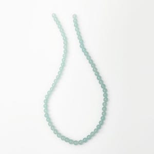 May include: A delicate necklace featuring small, round, pale green beads. The beads are strung together to form a necklace, creating a simple and elegant design. The necklace is displayed against a white background.