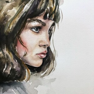 May include: A watercolor painting of a person in profile, featuring dark brown hair with bangs, defined eyebrows, and soft pink cheeks. The artwork uses shades of brown, grey, and muted skin tones on a textured white paper background with visible brushstrokes.
