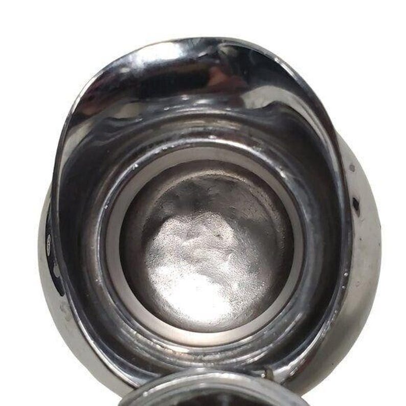 K&ouml;nnte beinhalten: Eine gl&auml;nzende, silberfarbene Metallkanne mit einem breiten, gebogenen Ausguss und einem abgerundeten K&ouml;rper. Der Innenraum ist sichtbar und zeigt eine glatte, reflektierende Oberfl&auml;che. Die Kanne scheint leer und sauber zu sein, mit einem einfachen, funktionalen Design.
