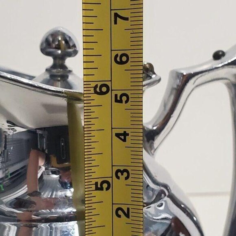 K&ouml;nnte beinhalten: Eine gl&auml;nzende silberne Teekanne mit Deckel und Griff, gemessen mit einem gelben Ma&szlig;band. Die Teekanne ist etwa 12,7 cm hoch, wie auf dem Ma&szlig;band angegeben.