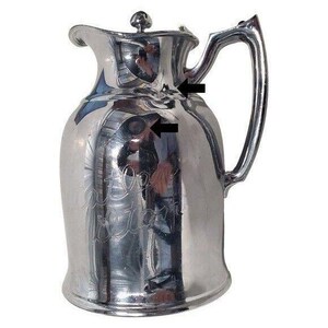 K&ouml;nnte beinhalten: Eine gl&auml;nzende silberne Kanne mit Deckel und gebogenem Griff. Die Kanne hat einen bauchigen K&ouml;rper und einen Ausguss. Die Oberfl&auml;che reflektiert die Umgebung. Die Kanne hat ein eingraviertes Design auf der Vorderseite.