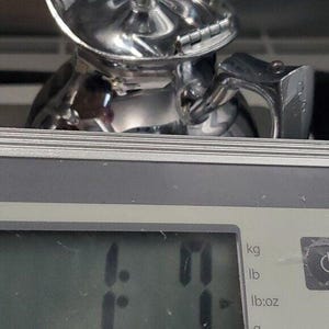 K&ouml;nnte beinhalten: Ein gl&auml;nzendes, silberfarbenes Metallobjekt, m&ouml;glicherweise ein Werkzeug oder Teil eines gr&ouml;&szlig;eren Mechanismus, liegt auf einer Digitalwaage. Die Waage zeigt ein Gewicht von 0,50 kg an. Das Objekt hat ein komplexes, geometrisches Design.
