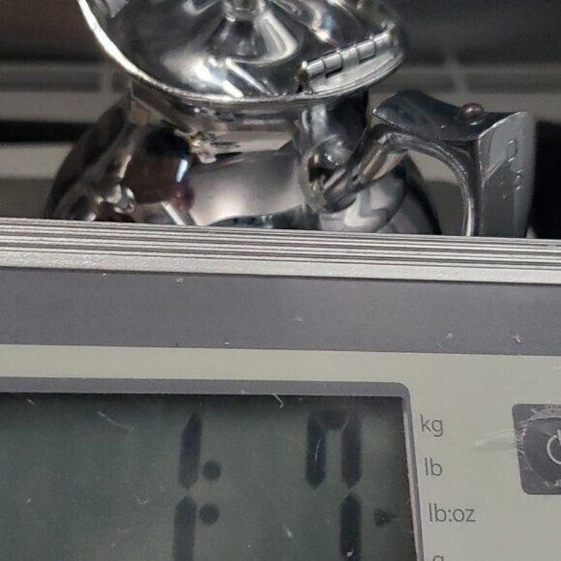 K&ouml;nnte beinhalten: Ein gl&auml;nzendes, silberfarbenes Metallobjekt, m&ouml;glicherweise ein Werkzeug oder Teil eines gr&ouml;&szlig;eren Mechanismus, liegt auf einer Digitalwaage. Die Waage zeigt ein Gewicht von 0,50 kg an. Das Objekt hat ein komplexes, geometrisches Design.