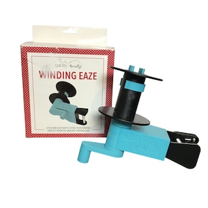 May include: A teal and black binding spooling tool with a crank handle and a black spool holder. The tool is next to a box with the text "WINDING EAZE" and a diagram of the tool. The box has a red and white polka dot pattern.
