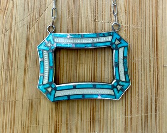 Puede incluir: Un collar de plata con un colgante rectangular de esmalte turquesa y blanco. El colgante tiene un diseño geométrico.