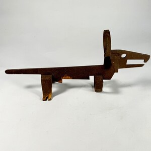 May include: A rusty metal sculpture of a dog, with a long body and a head with a large ear. The sculpture is made of flat pieces of metal that have been welded together.