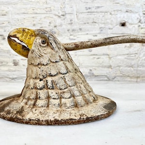 May include: A white cast iron nutcracker shaped like an eagle with a yellow beak and head. The eagle has a detailed design of scales on its body and a long handle.