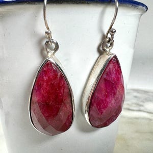May include: A pair of silver teardrop earrings with faceted ruby red stones.