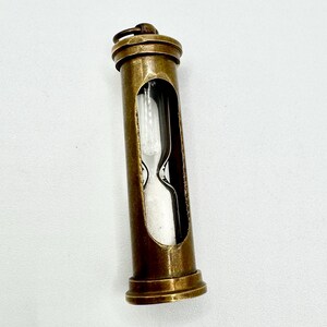 May include: A vintage brass hourglass with a clear glass chamber. The hourglass is encased in a cylindrical brass frame with a small loop at the top. The sand timer is a classic decorative item.