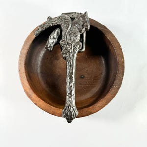 May include: A silver squirrel nutcracker with a detailed design, sitting in a wooden bowl.