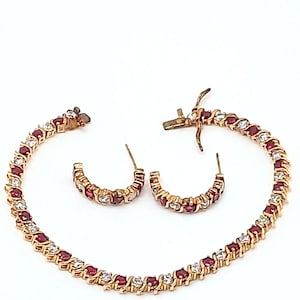 May include: A gold tone bracelet and earrings set with alternating red and clear stones.