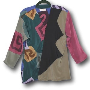 May include: A long-sleeved blouse with a patchwork design in various colors, including green, black, pink, and brown. The blouse has a V-neck and a loose fit. The fabric appears to be a silky material. The blouse is hanging on a green hanger.