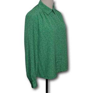 May include: Green long-sleeve blouse with a collared neckline. The blouse features a pattern of small white and dark blue dots on a green background with vertical stripes. The blouse is displayed on a mannequin.
