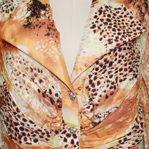 May include: A close-up of a yellow, orange, and brown patterned blouse with a button closure and rhinestones. The fabric has a crinkled texture.